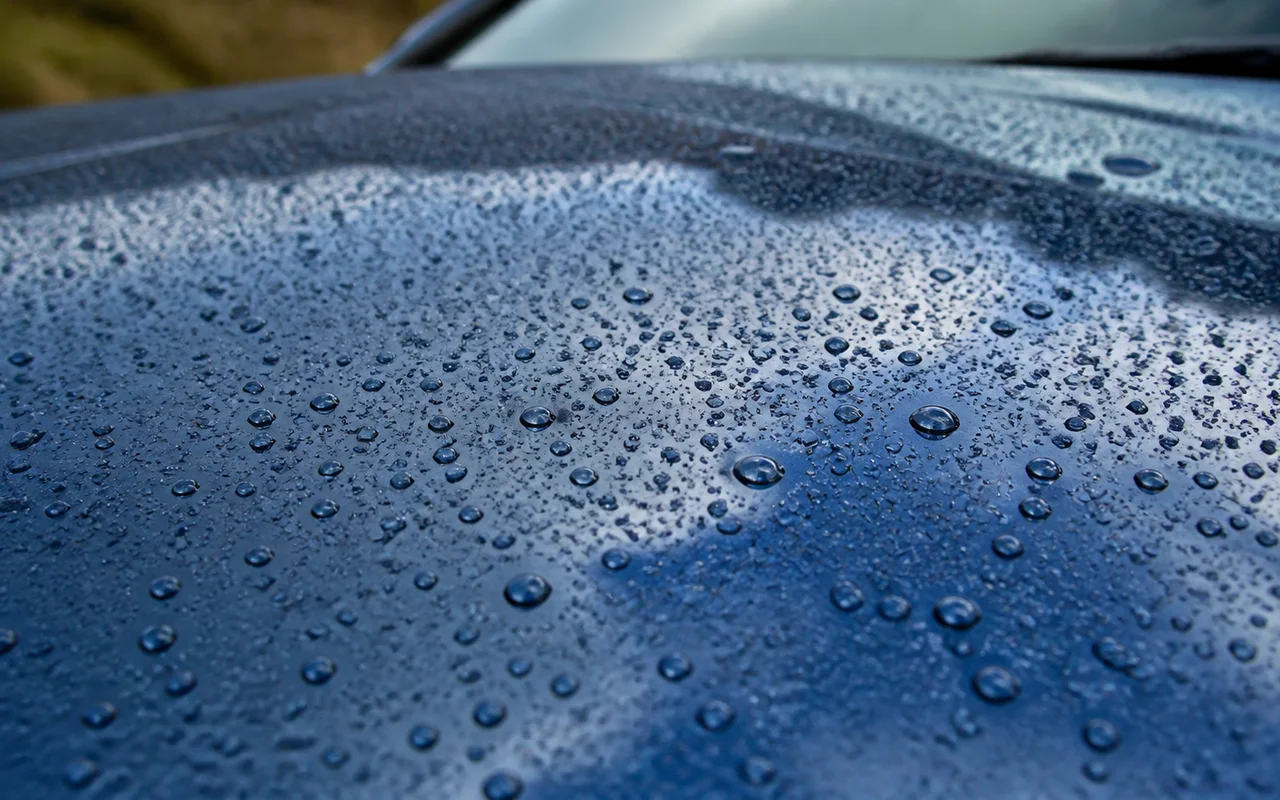 Close view of round water droplets across a glossy blue car hood