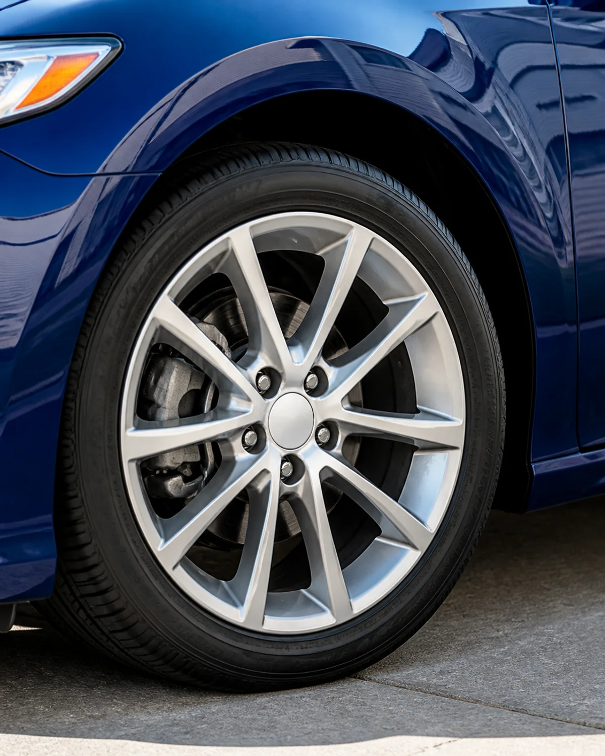 Close view of silver alloy wheel with plain center cap and glossy blue fender reflecting residential architecture